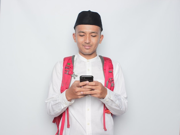 A man with a red backpack and a black hat is texting on his phone.