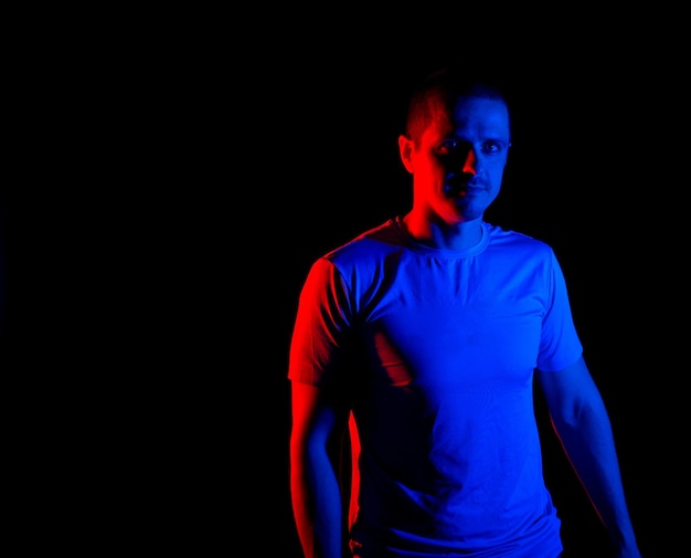 Man with red and blue light looking in camera standing in studio at black background