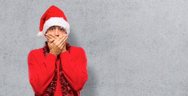 Uomo con vestiti rossi che celebra le feste di natale che coprono la bocca con entrambe le mani