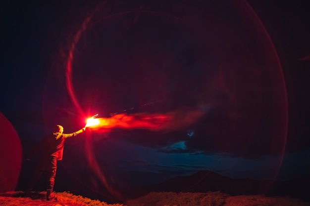 Foto l'uomo con un bastone rosso di fuochi d'artificio in piedi su una montagna di notte