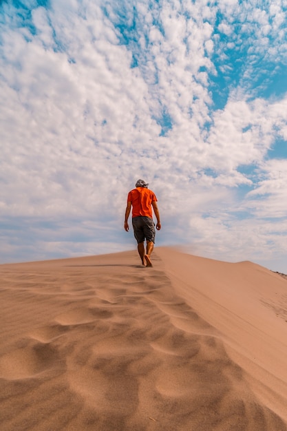 Photo a man with a red shirt and a turban on his head, walking in the desert of the dune