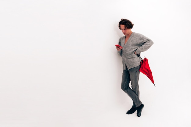 Man with red umbrella looking at cellphone in an empty white room