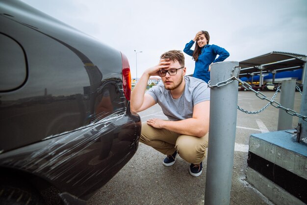 Man with sad look on scratched car woman with sorry look near dent auto insurance case