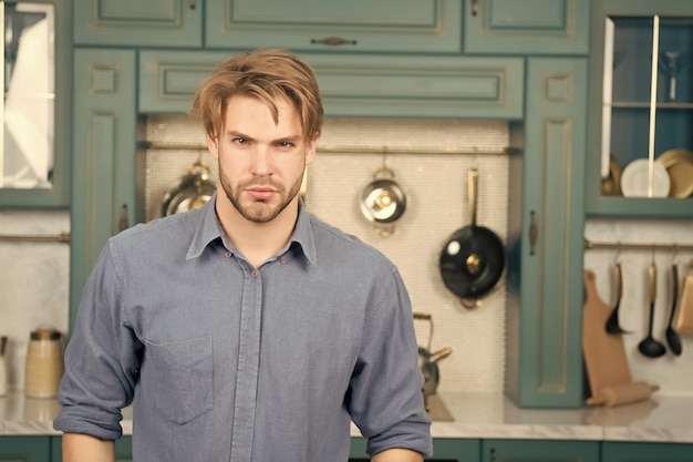 Мужчина с серьезным лицом, светлыми волосами в синей рубашке стоит на кухне Концепция приготовления пищи