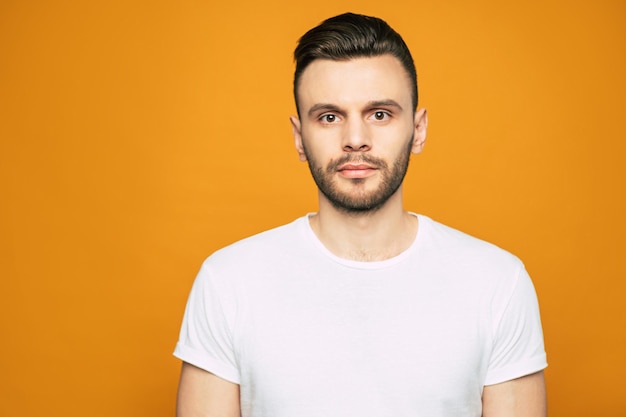 A man with a serious face is looking right into the camera with his big brown eyes clothed in basic white T-shirt