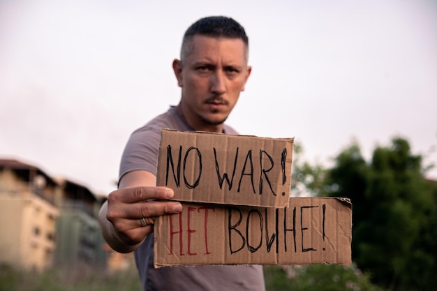 A man with serious and sad eyes holds a cardboard poster with the inscription NO WAR in English in h