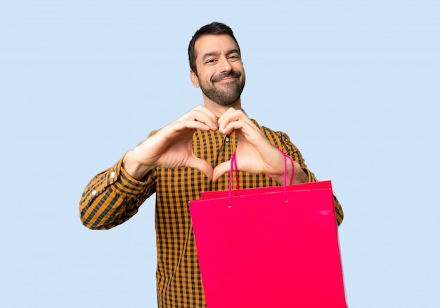 Man with shopping bags making heart symbol by hands on isolated blue background