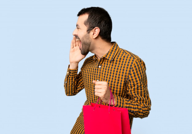 Man with shopping bags shouting with mouth wide open to the lateral on isolated blue background