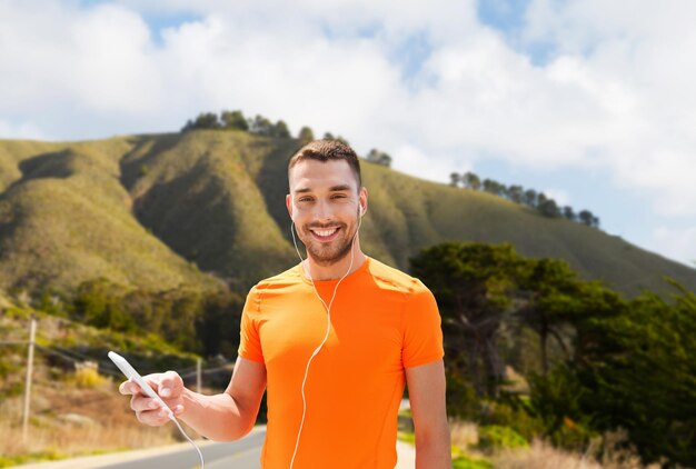 man with smartphone and earphones over hills