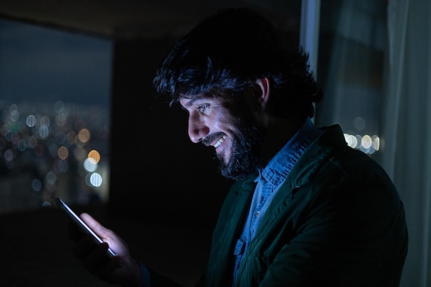 Человек с смартфоном в ночное время на балконе с видом на город концепция технологии мобильных телефонов