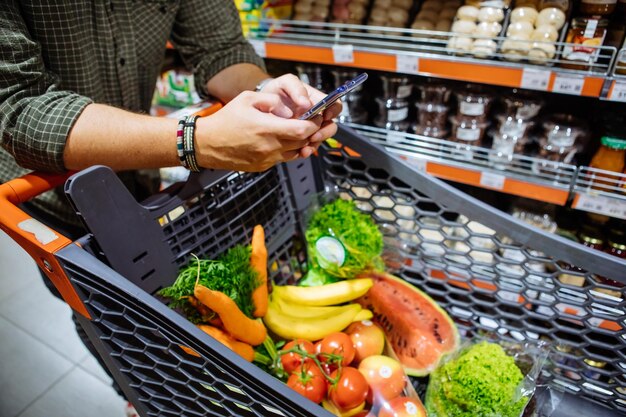 Мужчина со смартфоном делает покупки в продуктовом магазине