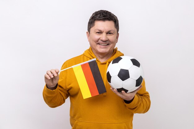 Man with smile holding flag of germany and soccer black and white classic ball and watching match