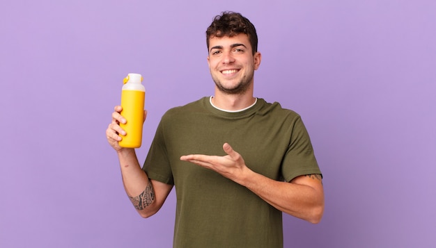 Man with smoothy smiling cheerfully, feeling happy and showing a concept in copy space with palm of hand