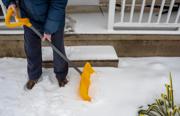 Мужчина с лопатой для снега чистит тротуар зимой Зимнее время снаружи