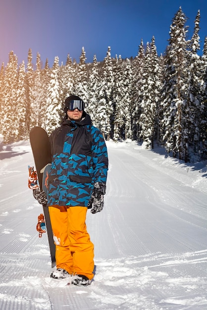 森を背景に屋外の雪の中にスノーボードを持った男が立っている