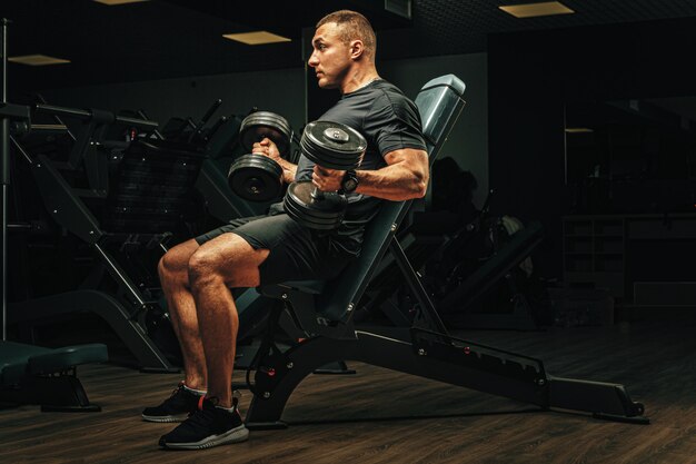 Man with sport body lifting dumbbells at the gym