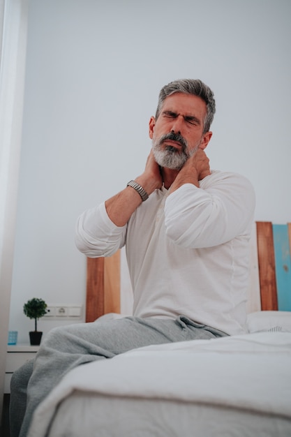 Man with suffering face in his 50s with neck pain in his bed