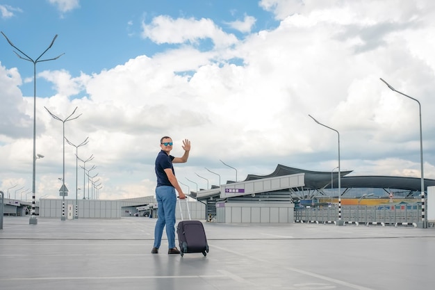 A man with a suitcase in an airport parking lot waving