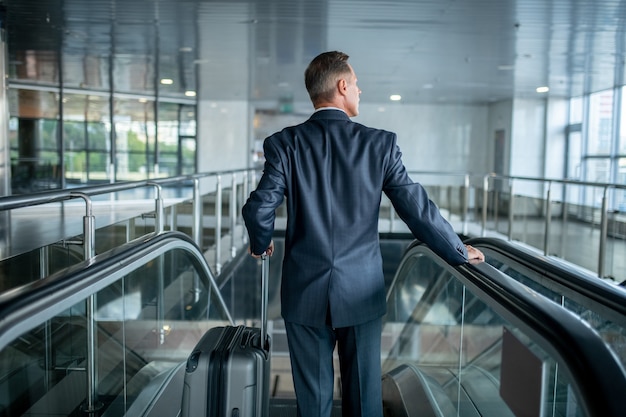 Man with suitcase on escalator with back to camera