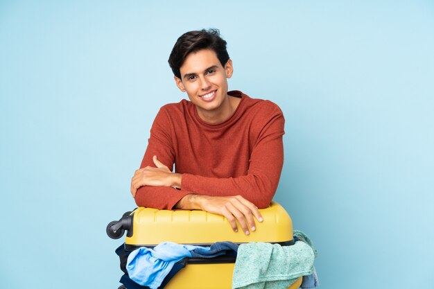 Man with a suitcase full of clothes over blue wall