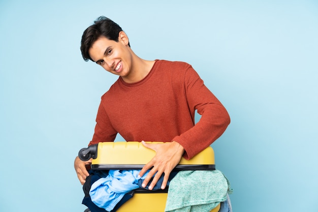 Man with a suitcase full of clothes over isolated blue wall