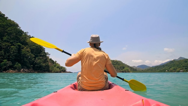 Man with sunglasses and hat rows pink plastic canoe along sea ag