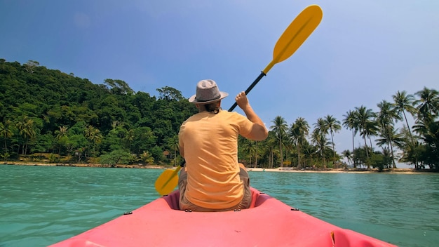 Man with sunglasses and hat rows pink plastic canoe along sea ag