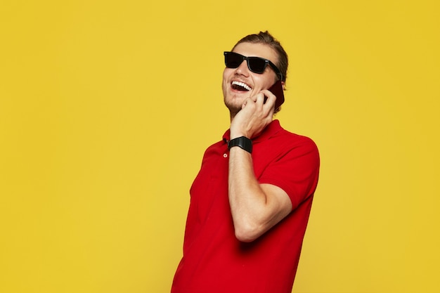 Man with sunglasses smiling and having phone call on yellow wall