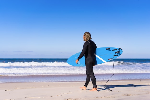 Foto uomo con tavola da surf sulla riva dell'oceano. surfer in una muta