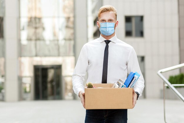 Man with surgical medical mask going out with cardboard looking at camera and feeling looser