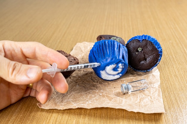 Man with syringe injecting insulin into moldy chocolate muffinside view