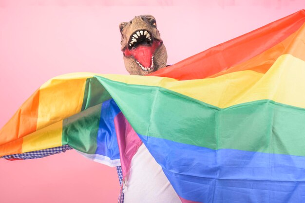 Foto uomo con testa di t-rex agita una bandiera arcobaleno su uno sfondo rosa isolato concetto surreale e divertente