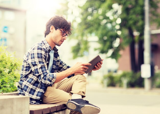 タブレットPCを持った男性が街のベンチに座っています