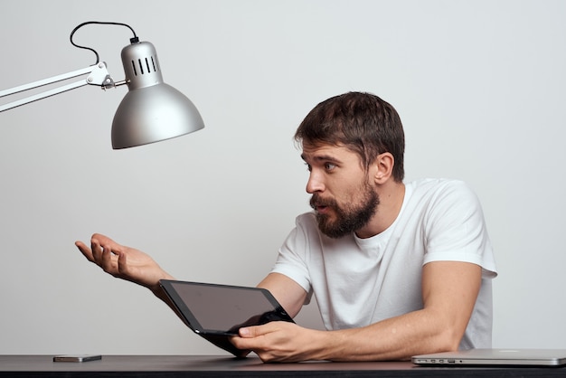 A man with a tablet at the table gestures with his hands on a\
light background and an iron lamp