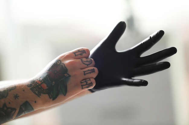 Man with tattoo wearing black latex gloves on blurred background