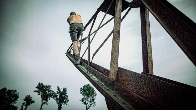 Man with tattooed body climbs on an old rustic crane and walks\
toward