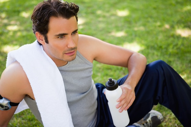 Man with a towel on his shoulder looking ahead while holding a sports bottle