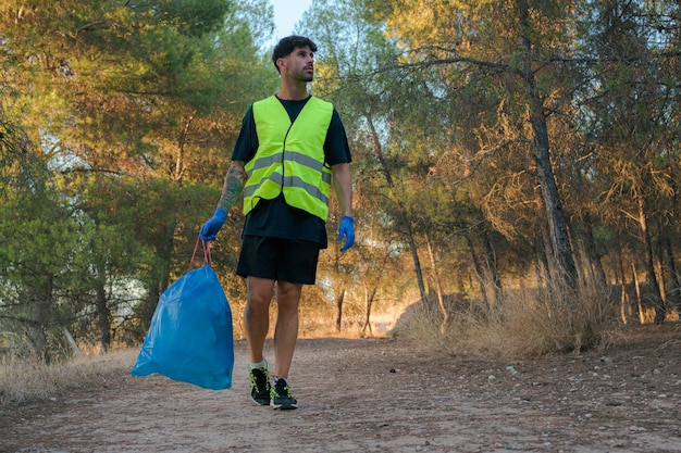 森の中でプラスチックでいっぱいのゴミ袋を持つ男