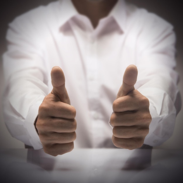 Man with two thumbs up at the background of a glossy table, concept image for illustration of excellence or best service.