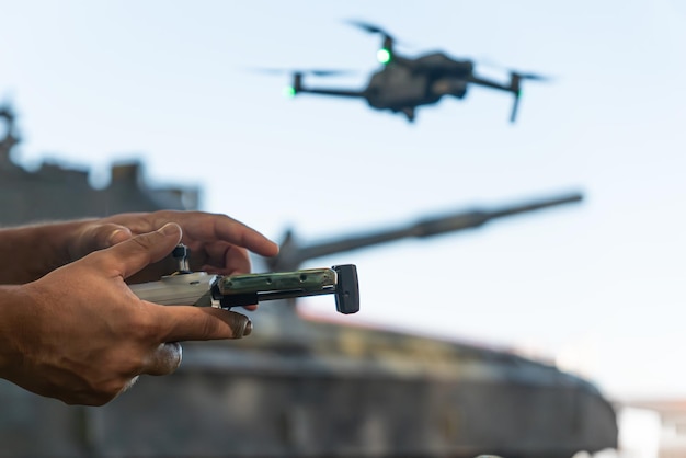 Photo a man with a uav control panel in his hands a drone flying above the tank in the background in nature help of reconnaissance drones in modern warfare