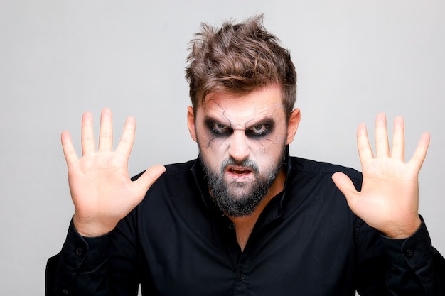 Foto un uomo con il trucco da non morto per halloween tiene le mani davanti a sé e guarda la telecamera da sotto la fronte