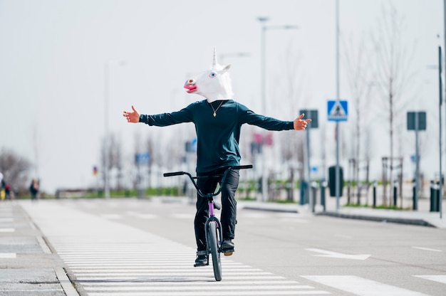 Foto uomo con maschera di unicorno in sella a una bicicletta