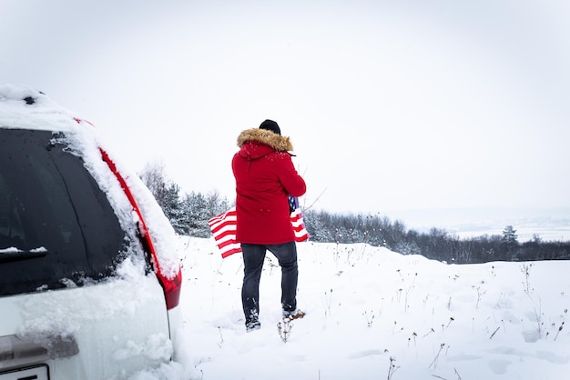 Man with usa flag in hands near suv car at top of snowed cliff.\
off road trip