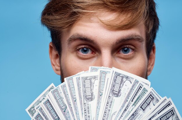 A man with a wad of money covers his face closeup blue background