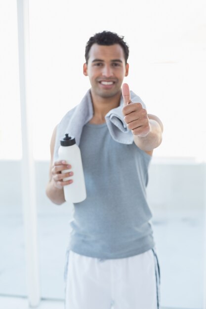 Man with water bottle and towel gesturing thumbs up in fitness studio