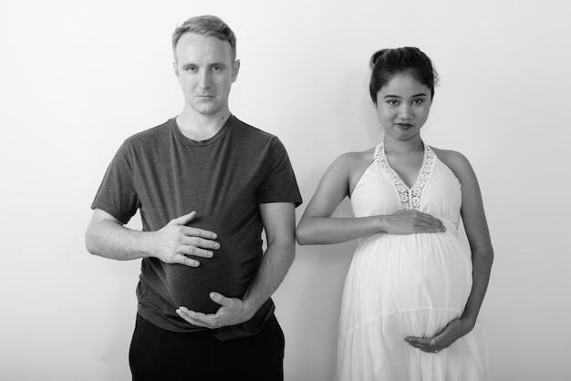 Uomo con l'anguria come stomaco e donna asiatica incinta insieme come coppia sposata multietnica in bianco e nero