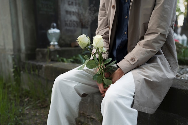 Человек с белыми розами на кладбище рядом с могилой