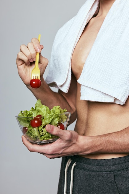 Мужчина с белым полотенцем на плечах держит тарелку салата, диета, здоровое питание. Фото высокого качества.