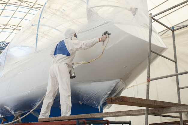 Man with white uniform spraying paint to the boat
