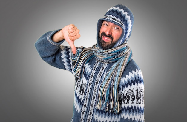 Man with winter clothes making bad signal on grey background